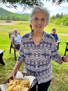 Nazair, Toni~ 2022, 07, 23 Glencoe, NB, with potato chips, husband Dave Eaton & her brother Georges in background- 01